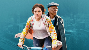 Foto de la protagonista de la película "Una buena persona" montada en una bicicleta con camisa de flores abierta. De fondo, el suegro de la chica con gorra gris.